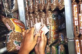 Retrato de mãos segurando dinheiro em frente a sacos de feijão nas prateiras do supermercado (Loc...