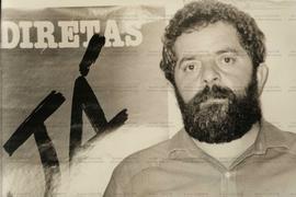 Lula, cadidato a Presidente pelo PT, posa para foto ao lado de cartaz das Diretas Já (Local desconhecido, [1987-1989]). / Crédito: Roberto Parizotti