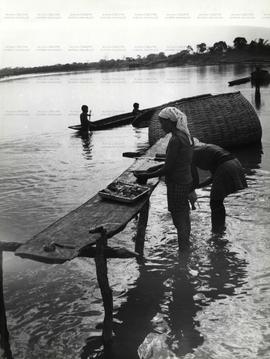 Mulheres limpam peixes à beira do rio (Local desconhecido, Data desconhecida). / Crédito: Silvest...