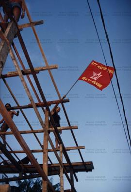 Homem segura bandeira do PT do alto de andaime (Local desconhecido, Data desconhecida). / Crédito: Autoria desconhecida.
