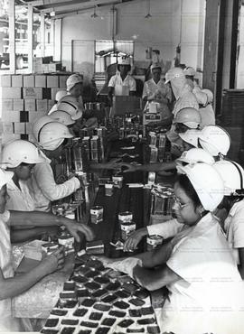 Mulheres trabalham em linha de produção de produtos alimentícios (Local desconhecido, Data descon...