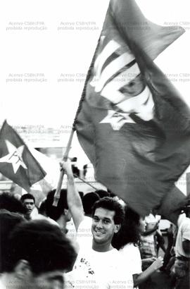 Jovem militante sorri empunhando bandeira em passeata, durante a campanha de 1989 (Recife-PE, 1989).  / Crédito: Eliane Velozo .